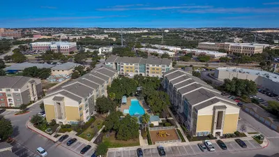 Inviting aerial view of a modern apartment complex featuring a sparkling central pool, lush landscaping, and spacious residential buildings, set in a vibrant urban area.