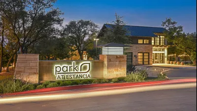 Elegant entrance of Park at Estancia, illuminated at dusk, featuring modern architecture amidst a lush, serene landscape.