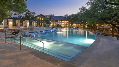 Stunning apartment complex with a luxurious outdoor pool, surrounded by lounge chairs and vibrant evening lights, perfect for relaxation and entertainment.