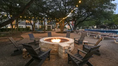 Charming outdoor seating area with a cozy fire pit surrounded by Adirondack chairs, under twinkling string lights in a serene community park.
