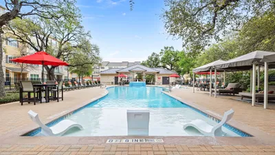 Inviting outdoor pool area with relaxing lounge chairs, vibrant red umbrellas, and lush greenery, perfect for leisure and entertainment.