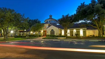 Inviting evening view of a charming apartment complex with elegant architecture and lush landscaping, highlighted by soft outdoor lighting.