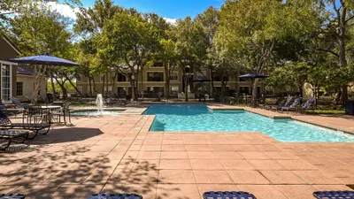 Inviting outdoor pool area with serene water fountains, surrounded by lush trees and comfortable lounge chairs for relaxation.
