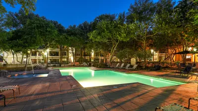 Charming residential outdoor scene featuring a sparkling illuminated swimming pool surrounded by lush trees and elegant apartment buildings.