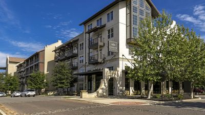 Elegant apartment building with modern design and balconies, surrounded by lush trees under a clear blue sky.