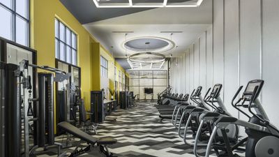 Modern apartment fitness center featuring state-of-the-art cardio machines and sleek strength training equipment, set in a stylish space with vibrant yellow accents.