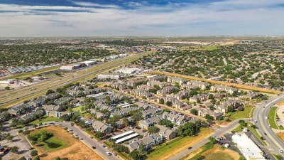 Breathtaking aerial view of modern apartment complex surrounded by lush greenery and conveniently located near major highways.