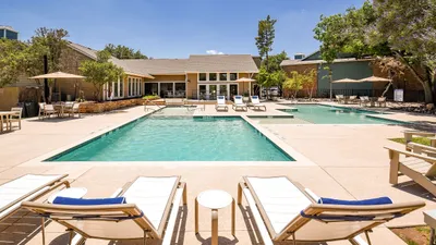 Luxurious apartment complex featuring a sparkling outdoor pool, surrounded by comfortable lounge chairs and shaded seating areas, offering a perfect retreat for relaxation and leisure.