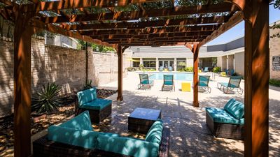 Inviting outdoor area with cozy seating under a wooden pergola, overlooking a sparkling swimming pool and sun loungers.