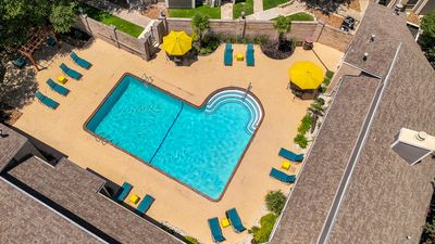Stunning aerial view of a vibrant community pool area with inviting turquoise water, surrounded by comfortable lounge chairs and cheerful yellow umbrellas, perfect for relaxation in a serene setting.