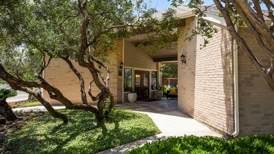 Charming apartment entrance framed by lush greenery and elegant trees, leading to inviting outdoor seating.