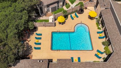 Inviting aerial view of a stylish apartment complex featuring a sparkling swimming pool with ample sun loungers and vibrant yellow umbrellas, surrounded by lush greenery.