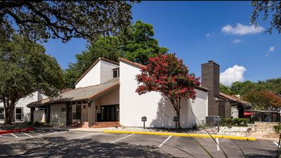 Charming residential building with a picturesque courtyard, vibrant landscaping, and ample parking under a clear blue sky.
