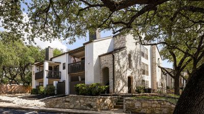 Charming apartment building surrounded by lush greenery, featuring rustic stone accents and spacious balconies, offering a serene living experience.