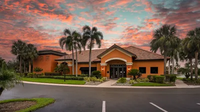 Charming apartment complex exterior with vibrant landscaping and palm trees, set against a stunning sunset sky.