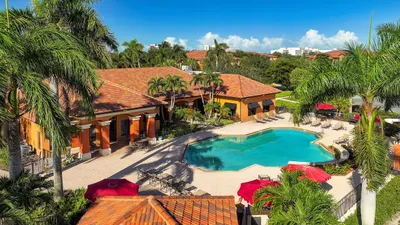 Lush tropical retreat featuring a vibrant community clubhouse with a stunning pool, surrounded by palm trees and inviting lounge areas under sunny skies.