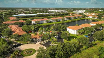 Aerial view of a charming apartment complex with terracotta roofs, lush greenery, and a tranquil pond in the center, offering serene suburban living.