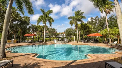Inviting tropical oasis with a sparkling pool surrounded by lush palm trees and cozy lounge areas under vibrant umbrellas.
