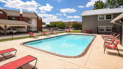Inviting apartment community pool with modern red loungers, surrounded by well-maintained landscaping and blue skies.
