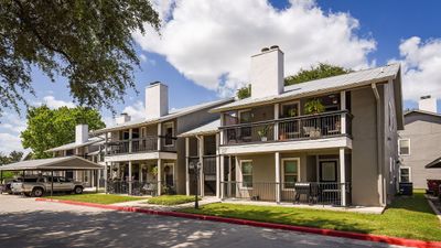 Charming apartment complex with private balconies, vibrant greenery, and ample parking under a sunny sky.