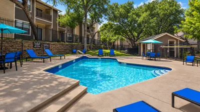 Inviting apartment complex featuring a sparkling blue swimming pool, shaded lounge chairs, and lush greenery, perfect for relaxation and outdoor enjoyment.
