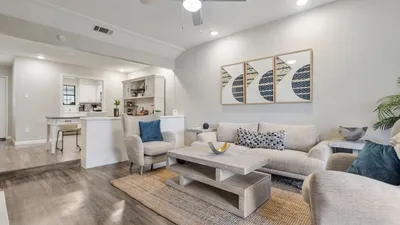 Bright and welcoming living room with modern decor, featuring comfortable seating, stylish artwork, and an open-concept design leading to a functional kitchen.