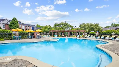 Inviting outdoor pool area featuring sun loungers, vibrant yellow umbrellas, and lush greenery under a bright blue sky.