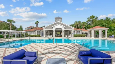 Luxurious outdoor pool area with stylish blue lounge seating, surrounded by lush greenery under a bright blue sky.