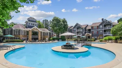 Inviting apartment community with elegant architecture, surrounded by lush greenery and featuring a sparkling, resort-style pool with lounge chairs and umbrellas.
