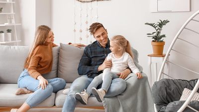 Cozy living room with a happy family seated on a modern gray sofa, surrounded by stylish decor and soft lighting.