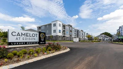 Inviting luxury apartment complex with modern architecture at Camelot at Edison, surrounded by lush landscaping and clear blue skies.