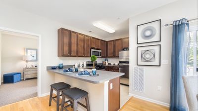 Modern kitchen with wooden cabinets, sleek countertops, and bar seating, opening into a beautifully decorated living area with elegant decor.