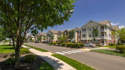 Charming apartment complex with manicured lawns, mature trees, and convenient parking under a clear blue sky.