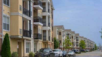 Elegant apartment complex with modern balconies, ample parking, and lush greenery along a quiet street.