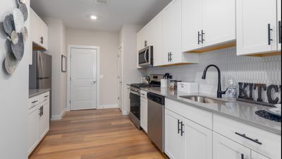 Modern kitchen with sleek white cabinets, stainless steel appliances, and elegant wooden flooring, exuding a bright and contemporary atmosphere.
