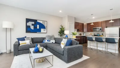 Modern open-concept living room and kitchen with sleek gray sectional, stylish decor, and elegant dining bar seating.