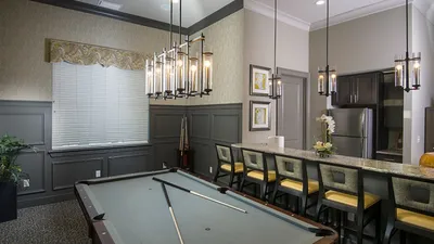 Chic apartment interior featuring a stylish billiard room with modern pendant lighting and a sleek kitchen bar with elegant seating.