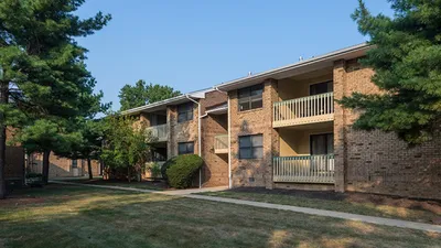 Charming brick apartment complex with private balconies, surrounded by lush green trees and manicured lawns.