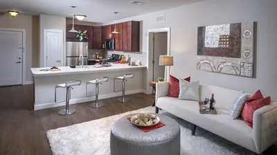 Modern open-concept living room and kitchen with elegant decor, featuring a cozy sofa, stylish artwork, and sleek bar stools around a spacious island.
