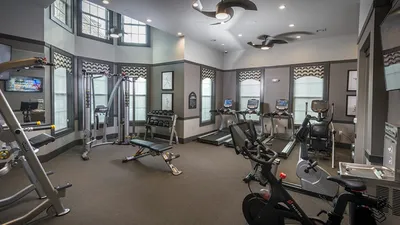 Luxurious apartment gym featuring modern cardio equipment, weight racks, and sleek design with ample natural light.