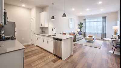 Modern open-plan kitchen and living room with stylish hardwood floors, sleek white cabinetry, and ample natural light.
