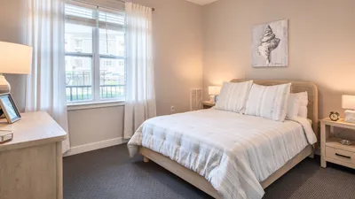 Bright and inviting bedroom with a cozy bed, elegant neutral decor, and a large window enhancing the airy ambiance.
