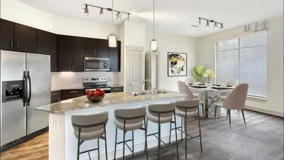 Modern kitchen with sleek dark cabinets, stainless steel appliances, and chic dining area featuring marble table and stylish chairs.