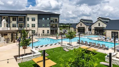 Luxurious apartment complex with a stunning outdoor pool, modern lounge chairs, and vibrant landscaped gardens under a bright blue sky.