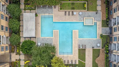 Stunning aerial view of a luxury apartment complex featuring a large, inviting swimming pool surrounded by lush greenery and stylish lounge areas.