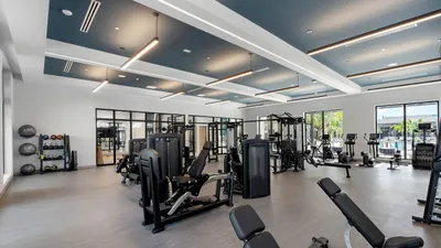 Modern, spacious gym with state-of-the-art equipment, bright windows, and sleek design for ultimate workout experience.