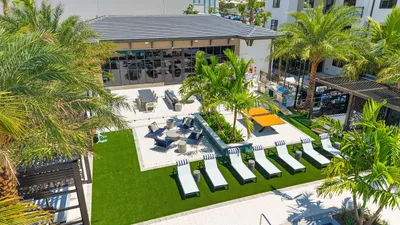 Vibrant outdoor recreation area with lush palm trees, stylish lounge chairs, and modern amenities in a luxury apartment complex.