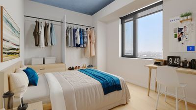 Serene bedroom with natural light, featuring organized open closet, cozy bed with vibrant blue accents, and a stylish workspace with city views.