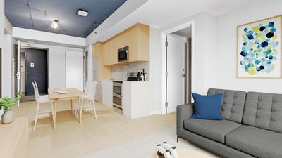 Modern open-plan living space with minimalist design, featuring a sleek kitchen with wooden accents, a cozy dining area, and a comfortable gray sofa with colorful wall art.