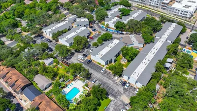 Vibrant aerial view of a modern apartment complex with lush greenery, spacious parking, and an inviting swimming pool area, perfect for relaxation and urban living.